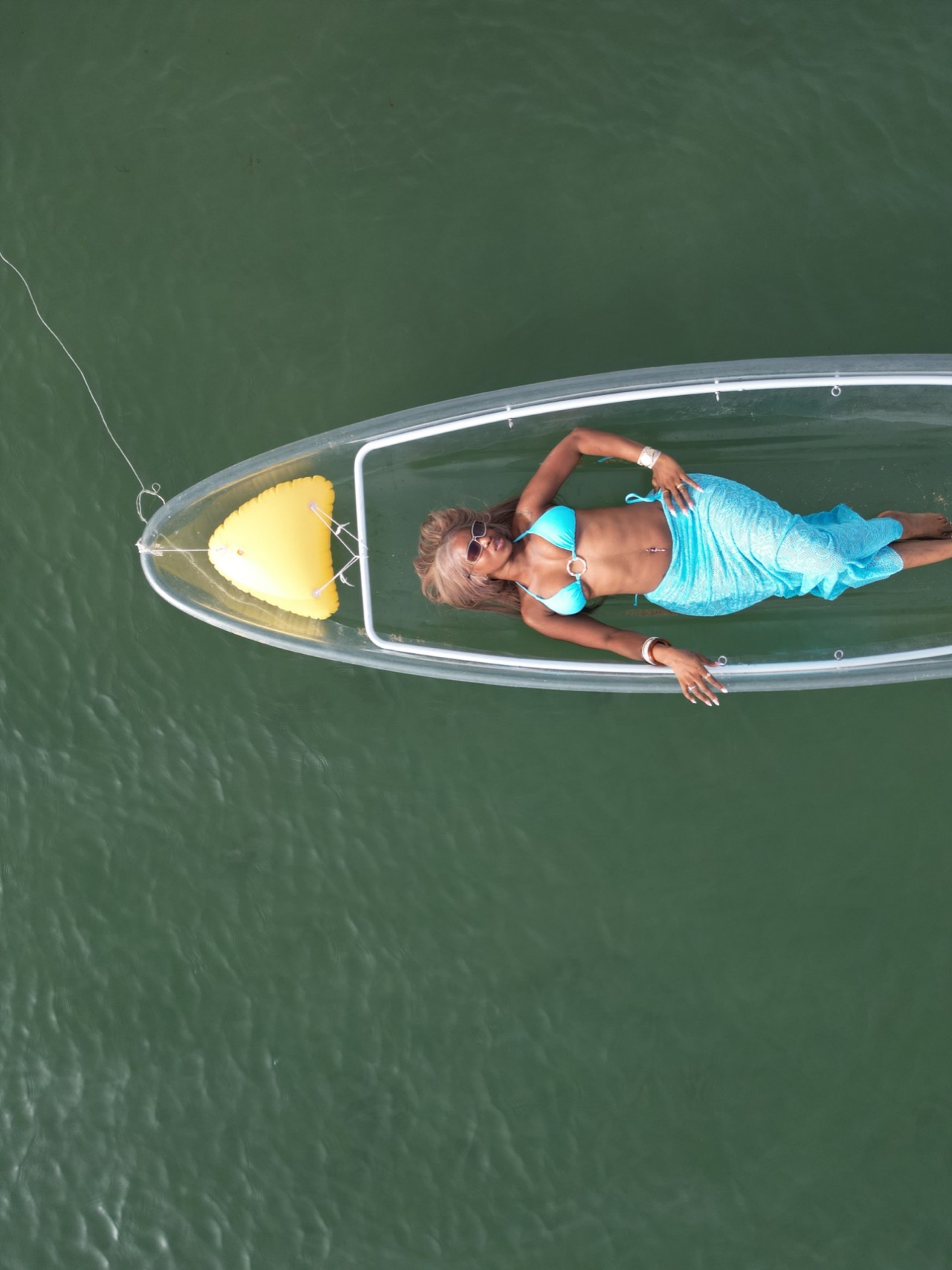 Shooting drone d’une cliente en maillot turquoise allongée dans un kayak transparent