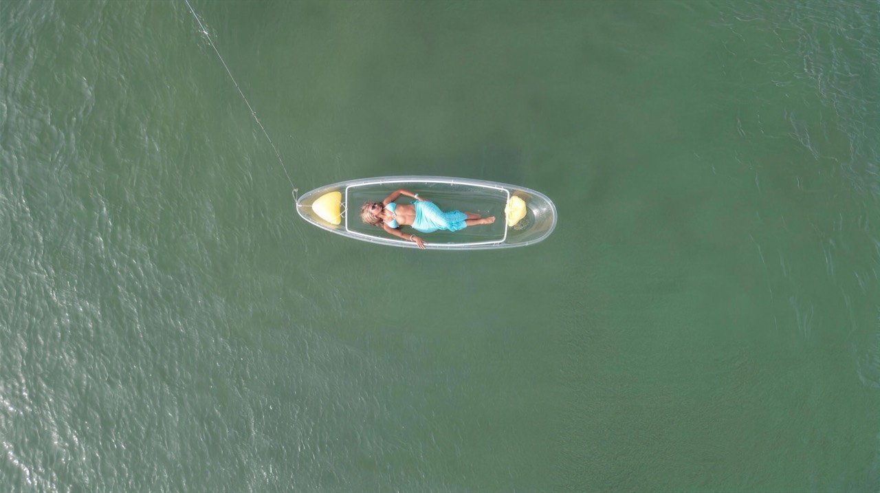 Cliente en tenue turquoise allongée dans un kayak transparent, vue du drone